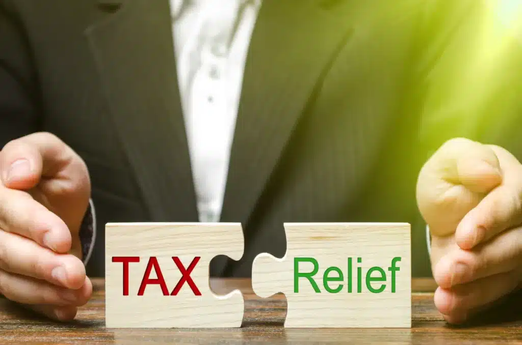 A businessman puts two puzzles with the words Tax and Relief. The concept of reducing the debt burden on business and local production to increase the competitiveness of their products. Economy