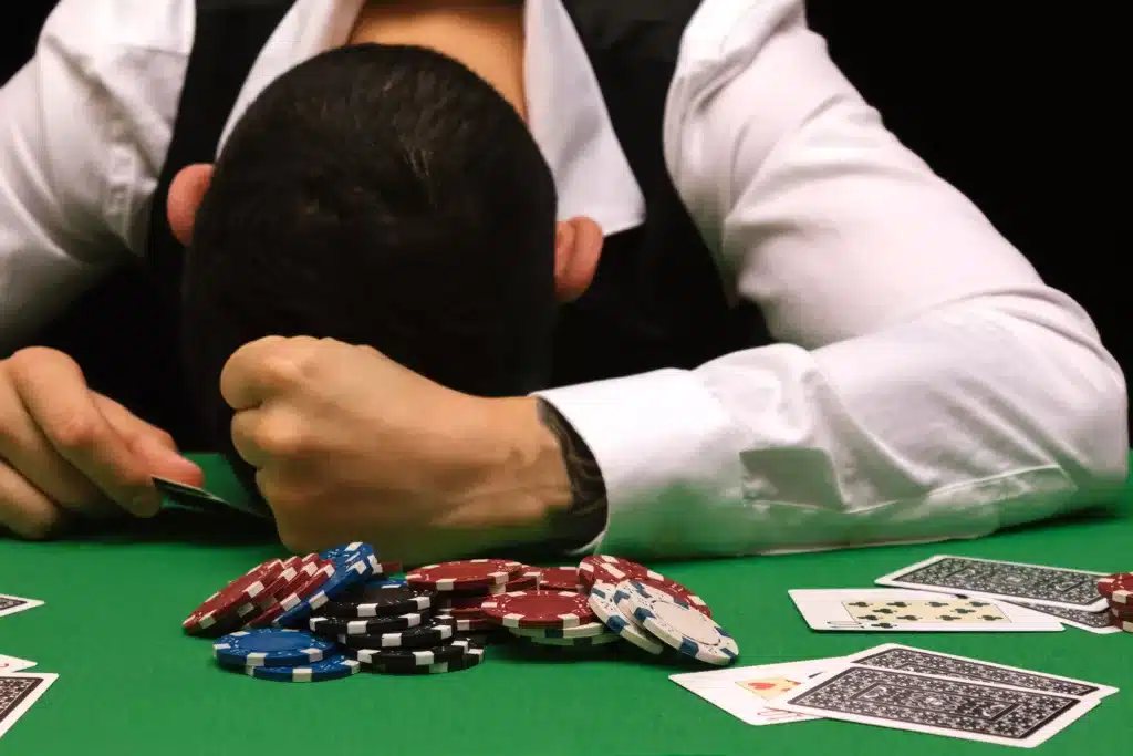 Devastated gambler man losing a lot of money playing poker in casino, gambling addiction. Divorce, loss, ruin, debt, gambling loss audit concept.